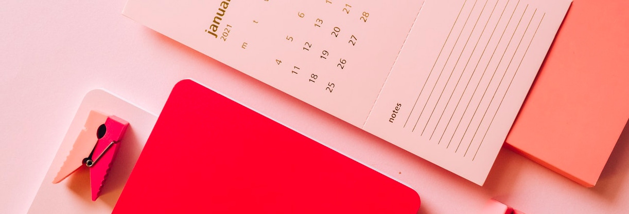 Un calendrier rose de janvier 2021 posé sur un fond rose à côté d'un carnet rouge pour faire la to do liste de son déménagement de bureaux