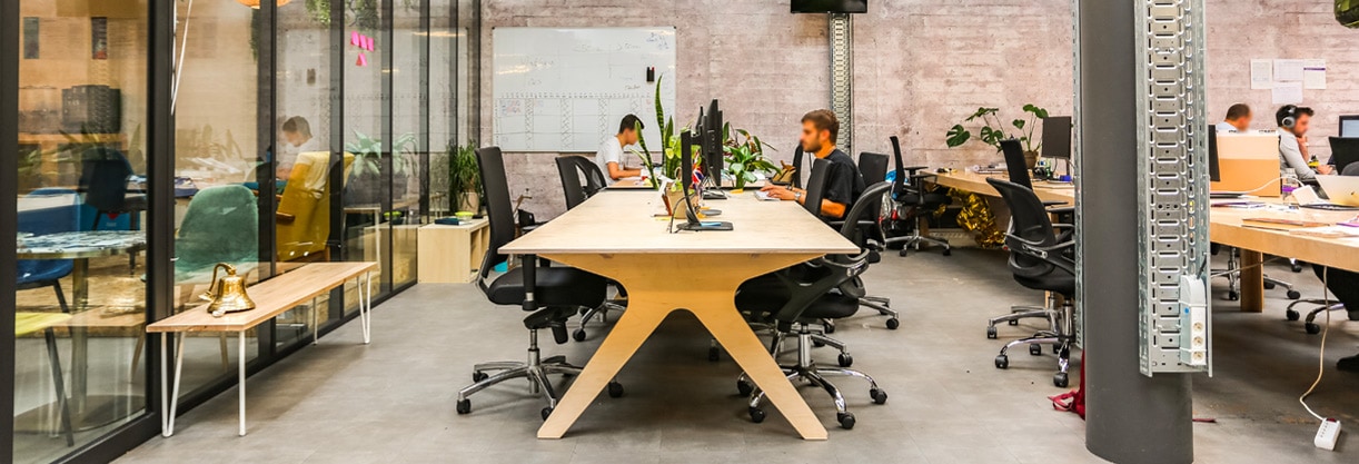 deux personnes travaillent sur du mobilier de bureau en bois dans un grand open space industriel