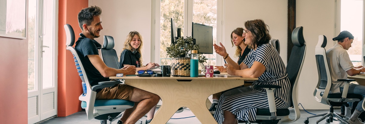 quatre personnes échangent autour d’un bureau en bois dans un espace de travail collaboratif en entreprise