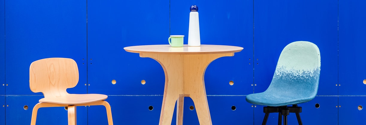 mobilier durable en bois pour entreprise avec une table ronde haute, une tasse, une gourde et deux chaises devant un mur bleu