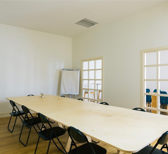 grande table de réunion en bois dans une salle avec des chaises noires et un chevalet