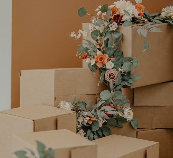 pile de cartons de déménagement devant un mur orange avec des fleurs blanches, roses, rouges et oranges posées dessus