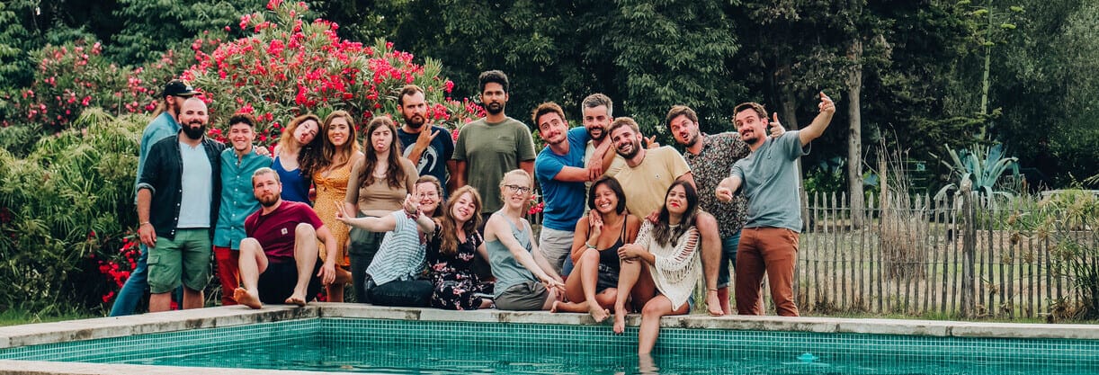 une vingtaine de personnes posent et s’amusent devant une piscine située devant une forêt