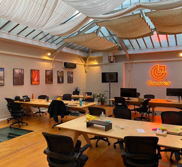 un open space avec des bureaux, sièges, fournitures et un néon orange sur le mur