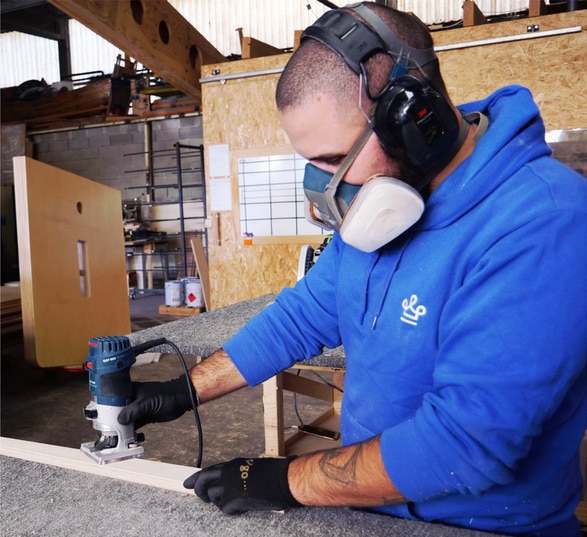 Homme en tenue LOUIS qui découpe une pièce de meuble en bois