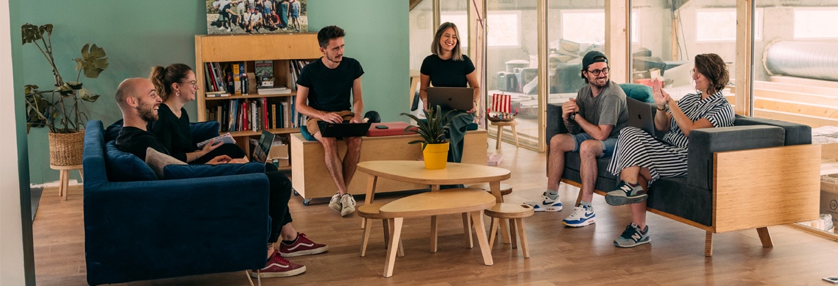 quatre collaborateurs heureux en entreprise sont assis sur des canapés et banquette dans un espace informel