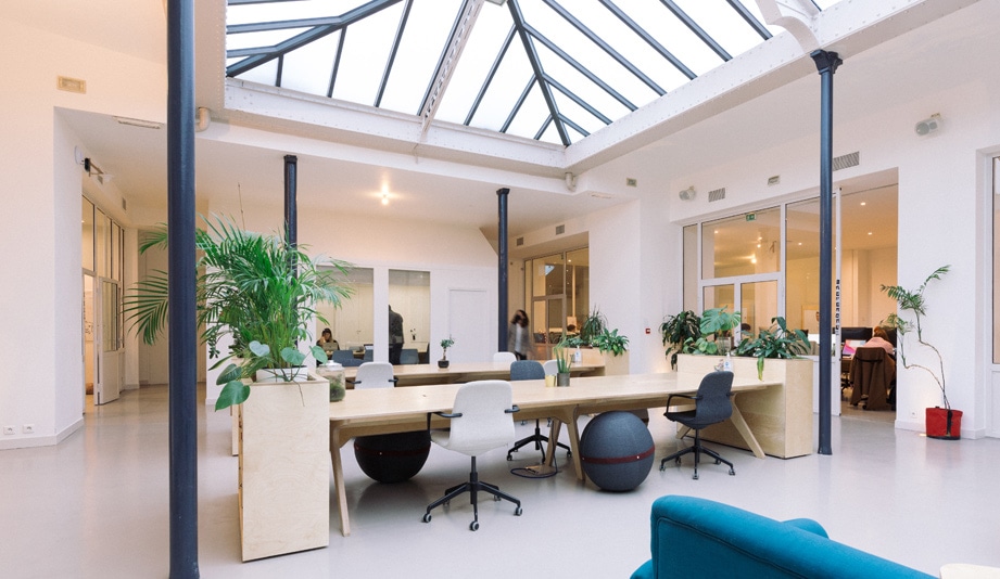 aménagement des bureaux d'atomic digital design à Paris avec des grandes tables en bois, des casiers de rangement, des sièges de bureau et une verrière