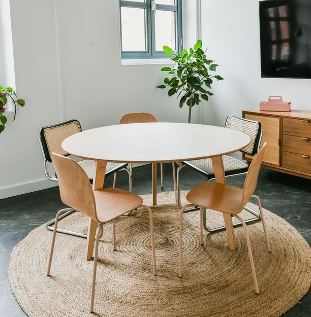 aménagement d’un espace détente en entreprise avec une table ronde en bois, des chaises, un tapis, une commode et une télévision murale