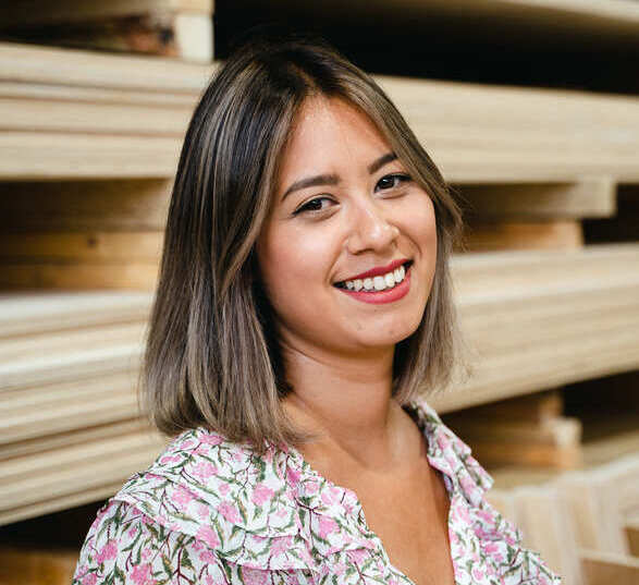 Jeune femme avec un carré court portant une blouse fleurie dans une atelier de production de mobilier en bois