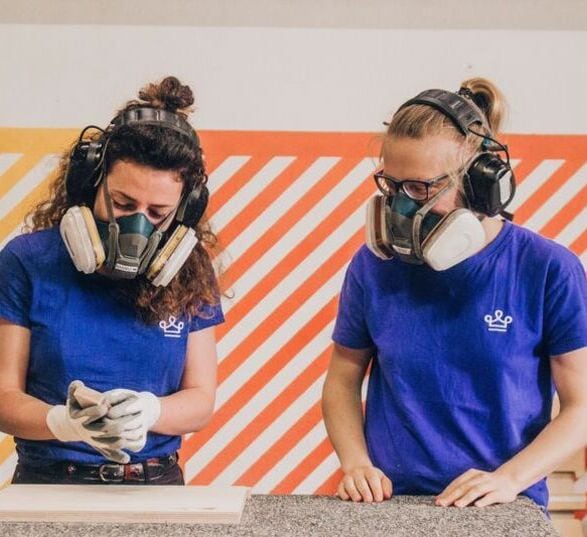deux femmes ébénistes avec des tee shirt bleus et des epi sont debout devant un établis