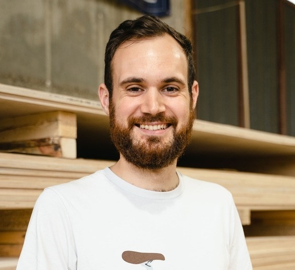 Homme brun avec un barbe portant un haut blanc dans une usine de bois