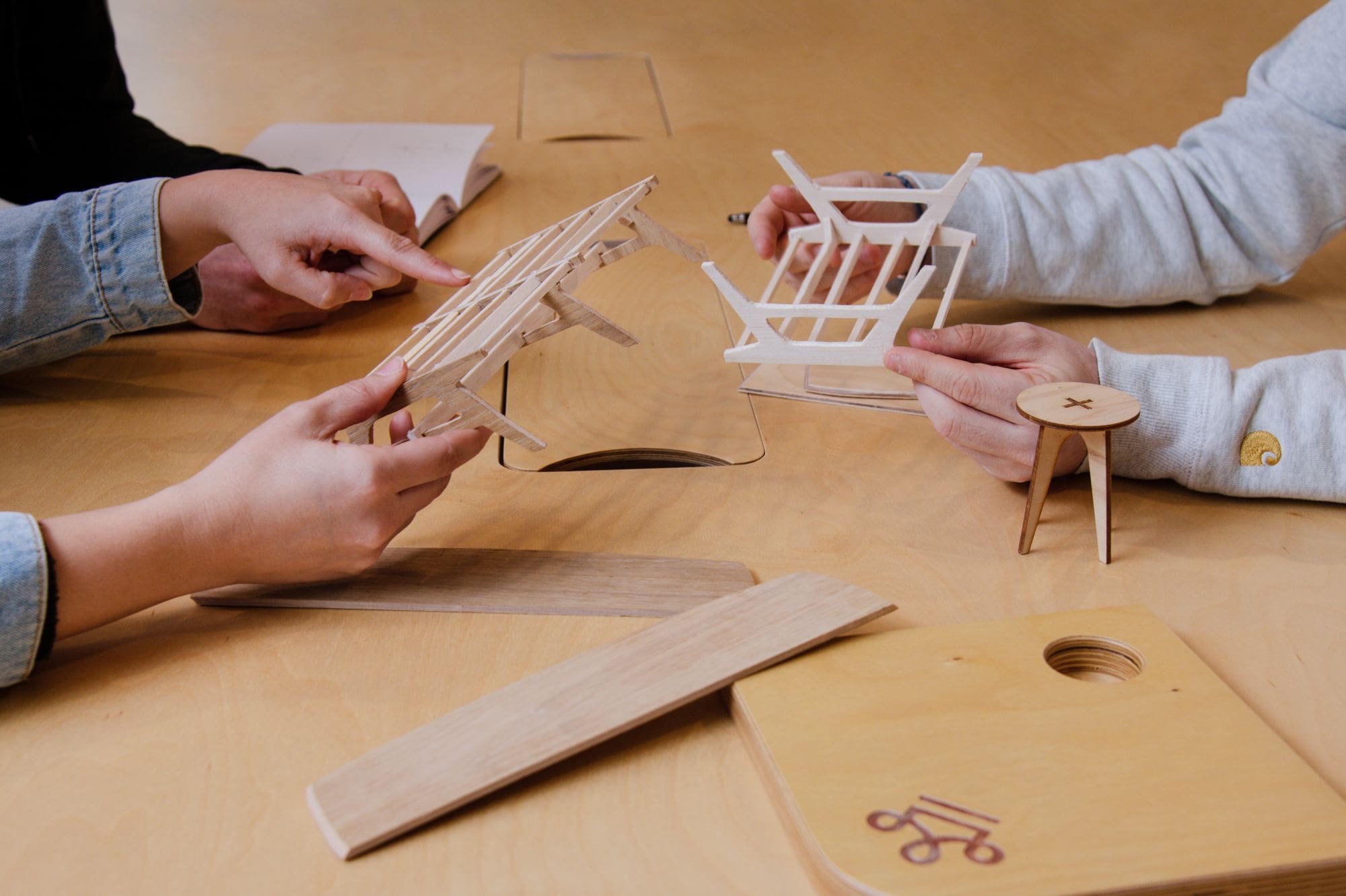 mains de trois personnes qui touchent des maquettes et échantillons en bois sur une table en bois claire