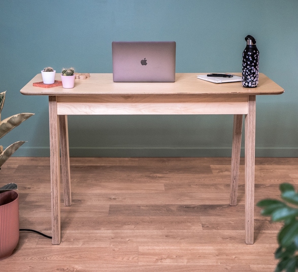 Petit bureau en bois clair dans une pièce avec un sol en bois et des murs vert entouré de plantes