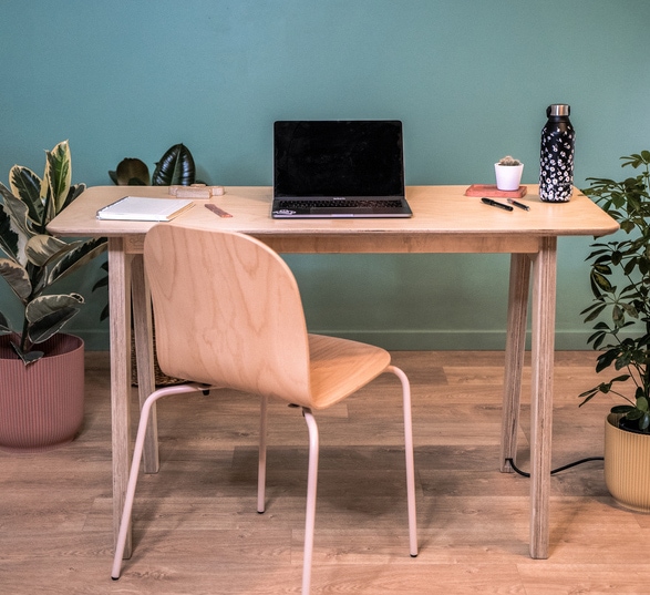 un ordinateur portable posé sur un petit bureau en bois clair dans une pièce avec un mur vert et des plantes