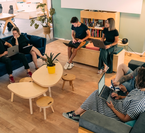 Six personnes travaillent dans un espace informel avec des canapés, tables basses et armoire de rangement