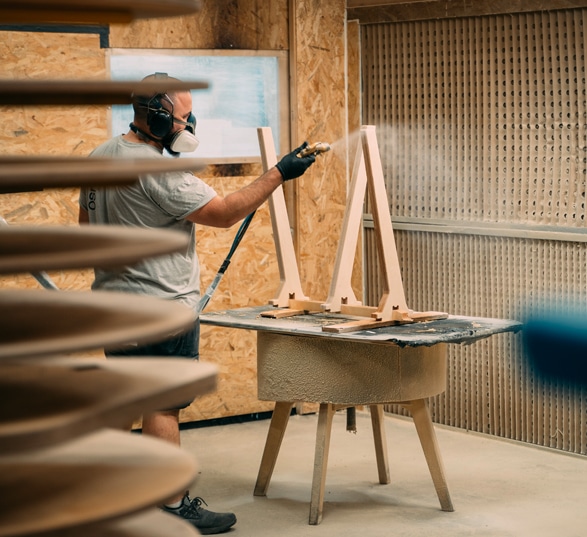 Un homme vernis un meuble en bois dans une cabine à vernis