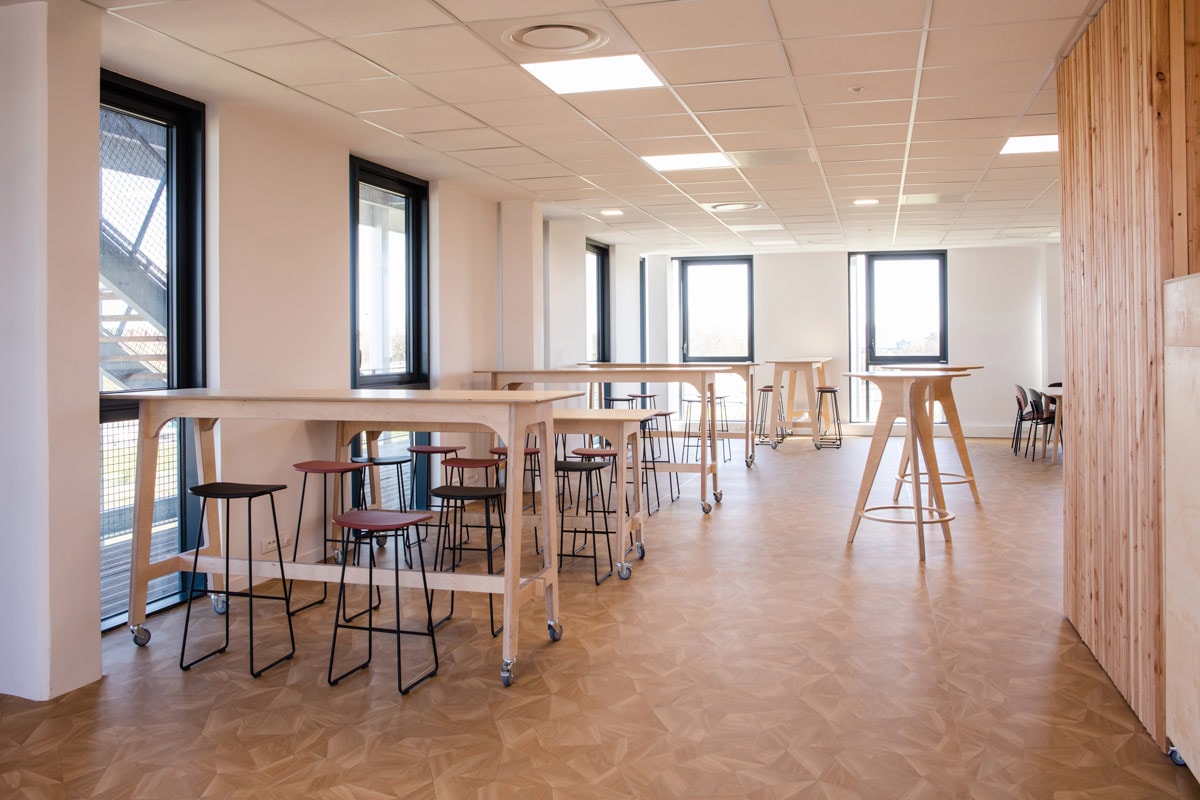 plusieurs chaises et tables hautes rectangulaires et rondes en bois dans une cafétéria d’entreprise