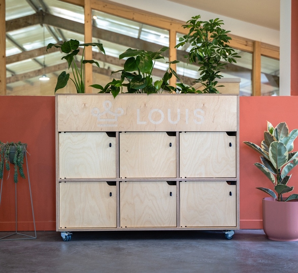 Meuble de rangement en bois avec des casiers individuels dans un open space avec un sol en béton ciré gris foncé et des murs orange