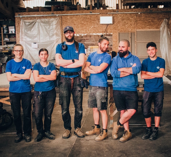 Six ébénistes debout dans un atelier de fabrication de mobilier de bureau à toulouse