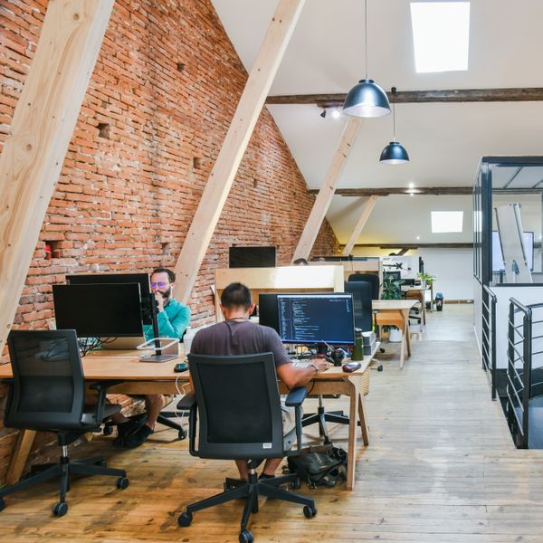 un espace de coworking avec bureaux partagés, siège de bureau, ordinateur et des murs en brique