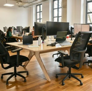 espace de travail en open space avec des grands bureaux en bois, des écrans d’ordinateurs et des sièges ergonomiques noirs