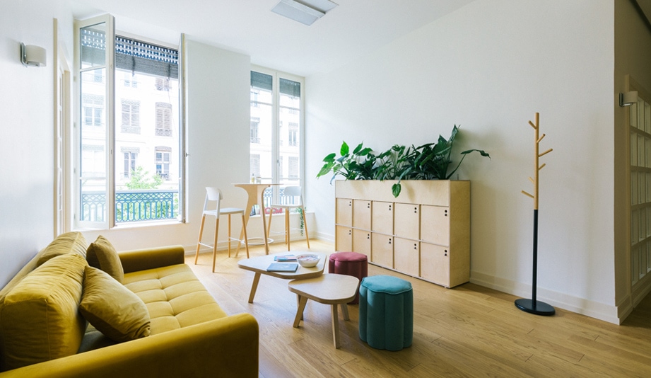un espace informel en entreprise avec canapé jaune, tables basses en bois, des poufs, un casier de rangement et une table haute