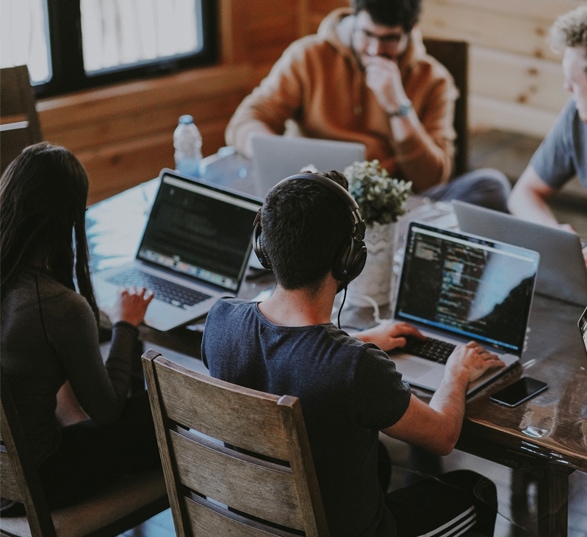 4 personnes travaillent sur un bureau avec leurs ordinateurs et casques audio