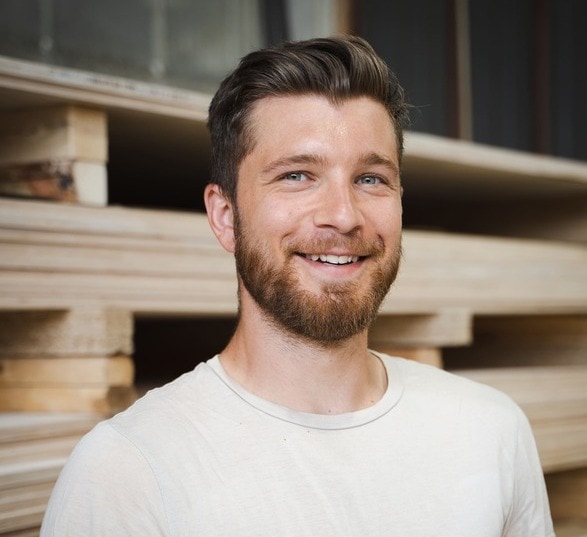 Jeune homme blond avec une barbe, souriant et portant un haut blanc 