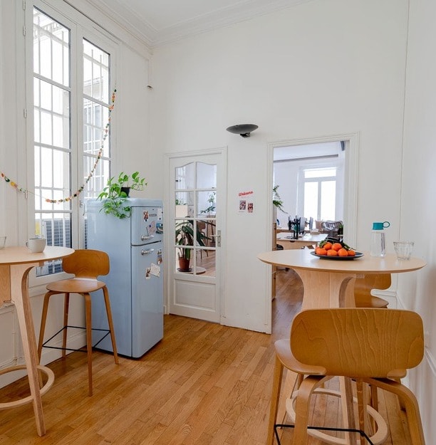 idée de salle de pause en entreprise avec table haute ronde, chaises hautes en bois et réfrigérateur bleu ciel