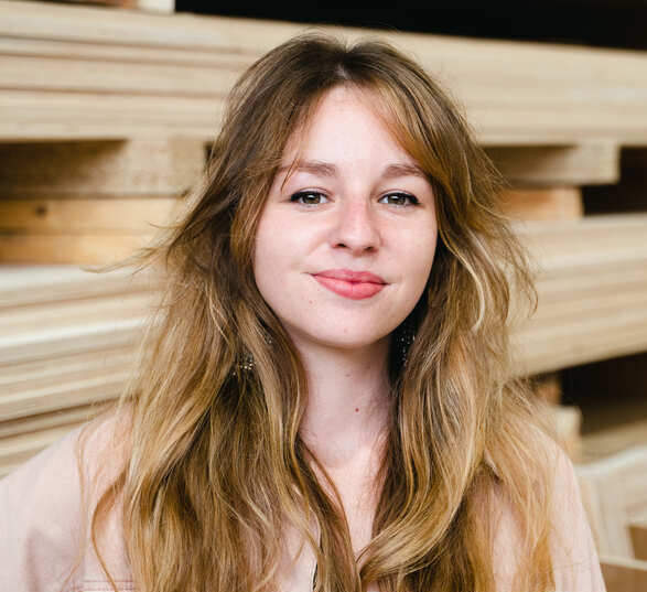 Jeune femme avec de longs cheveux blonds portant une veste rose dans un atelier d’ébénisterie 