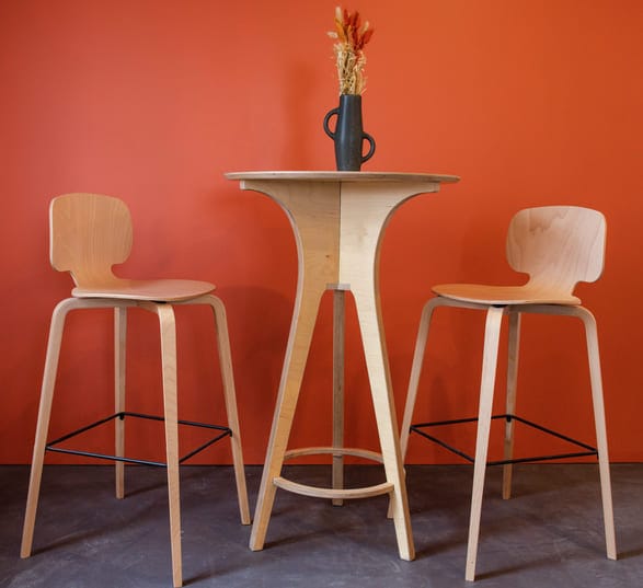 un table haute en bois type mange debout avec deux chaises et un vase de fleurs séchées dans une pièce peinte en orange