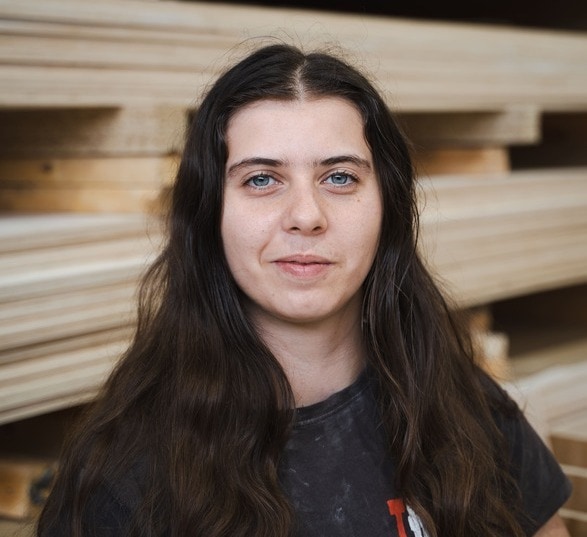 Jeune femme brune avec les yeux bleu portant un haut noir dans une usine de fabrication en bois
