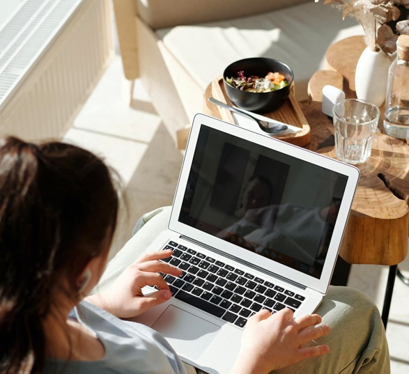 une femme télétravaille sur son ordinateur et elle est assise devant une table basse en bois