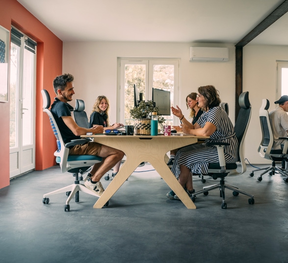 quatre personnes discutent autour d’un bureau en bois dans un open space au mur orange