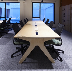 un open space office meublé avec une grande table de travail collaborative et des sièges de bureau noirs