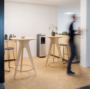 une personne marche dans une petite salle de pause d’entreprise équipée d’une machine à café et deux tables rondes hautes