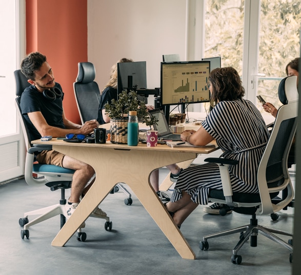 deux personnes discutent autour d’un bureau bench dans un open space au mur orange