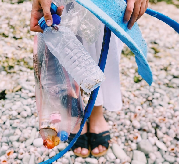 une personne ramassent des déchets et du plastique sur une plage avec des cailloux