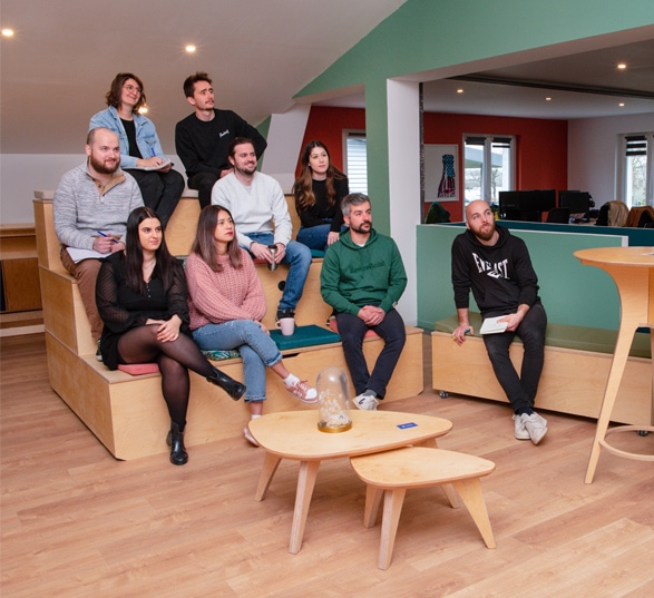 9 personnes sont assises sur une estrade et une chaise devant une table basse en bois