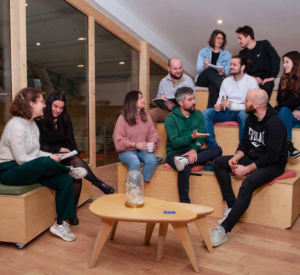 10 personnes sont assises et discutent sur une estrade en bois et une banquette avec une table basse gigogne devant eux