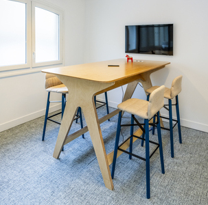 salle de réunion avec une table haute en bois connectée, des chaises hautes et une télévision murale