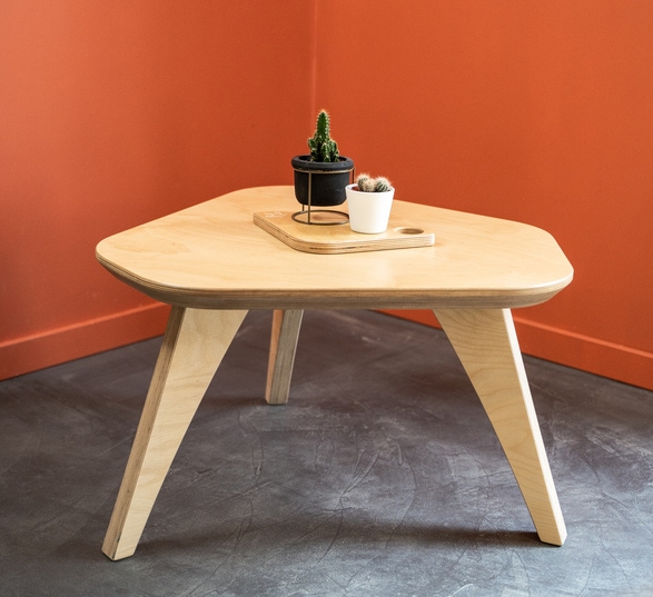 Petite table basse en bois clair avec un vase blanc posé sur le plateau dans une pièce aux murs orange et sol en béton ciré