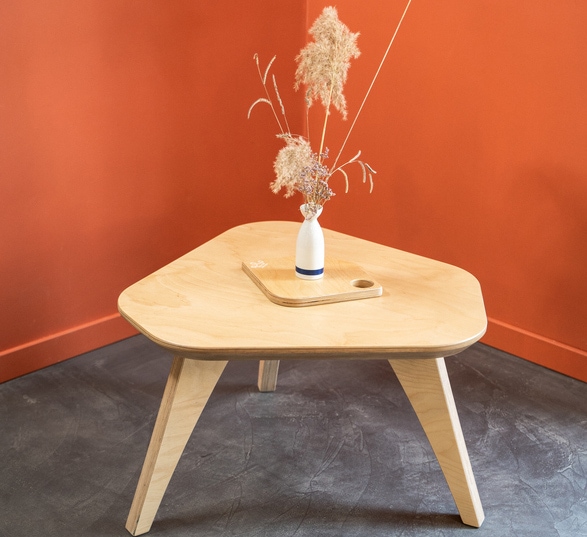 table basse en bois clair avec un vase blanc dans une pièce avec des murs oranges et un sol en béton ciré gris foncé