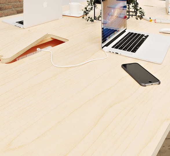 Deux ordinateurs portables et un smartphone sont posés sur une table de conférence design en bois équipée d’une goulotte centrale avec trappe
