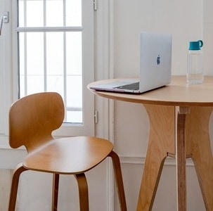 un ordinateur et une gourde sont posés sur une table ronde haute en bois avec une chaise haute devant
