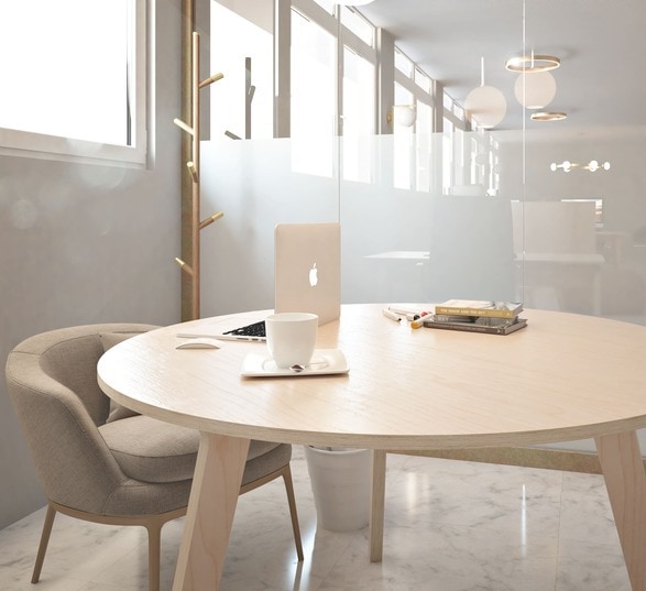 un ordinateur et une tasse à café posés sur une table de réunion ronde en bois clair dans une salle de réunion