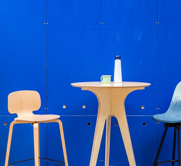 une table ronde haute design avec deux chaises devant un mur bleu
