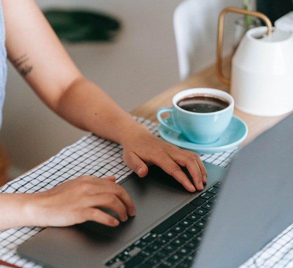 une personne télétravaille sur son ordinateur avec une tasse à café bleu posée à côte