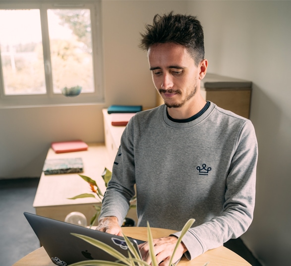 un homme travaille debout sur son ordinateur qui est posé sur une table haute ronde