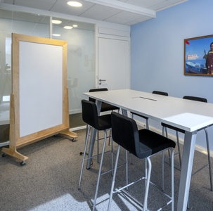 une salle de réunion avec table blanche, chaises noires et un tableau blanc en bois sur roulettes